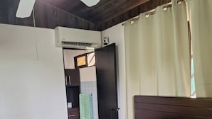 Ein Schlafzimmer mit Bett, Deckenventilator, Klimaanlage, einem Metallregal und einer Tür zu einem anderen Raum.