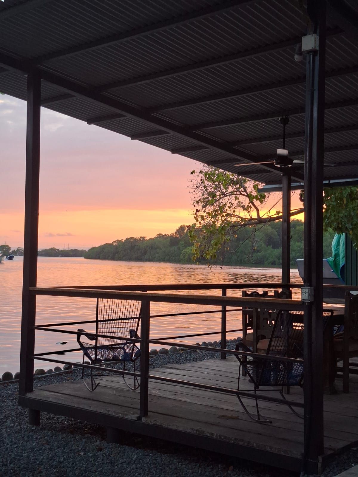 Un espacio de estar al aire libre cubierto con vista a un cuerpo de agua tranquilo y un atardecer.