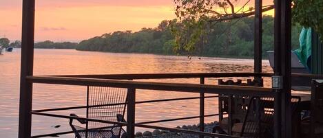 Un espacio de estar al aire libre cubierto con vista a un cuerpo de agua tranquilo y un atardecer.