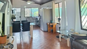 Ein geräumiger Wohnbereich mit hoher Decke, einem Deckenventilator und Blick zur Küche im Hintergrund.