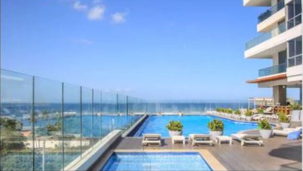 Una piscina sul tetto con vista libera sull'oceano, circondata da ringhiere in vetro e poltrone relax.