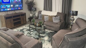 Un salon avec un téléviseur à écran plat diffusant le film « Les Gardiens de la Galaxie », un canapé gris, une table basse agrémentée d’objets décoratifs et un meuble en bois.