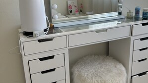 Une coiffeuse blanche avec un grand miroir, de nombreuses lampes et un tabouret moelleux.