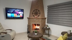 Un salon avec une cheminée en briques, un téléviseur fixé au mur et un canapé avec des coussins.