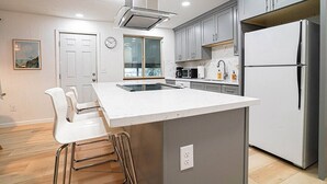 A modern kitchen with grey cabinets, a white island, stainless steel appliances, and a built-in oven.