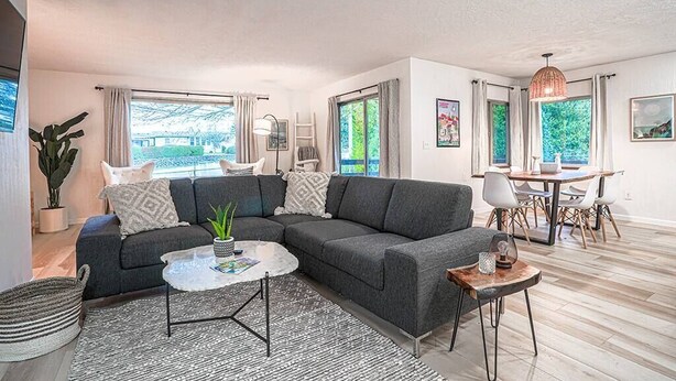 A modern living room with a grey sectional sofa, a round coffee table, and a dining area with a wooden table and chairs.