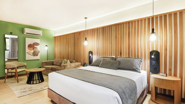 Un dormitorio moderno con una cama grande, un panel de madera con listones, una mesita auxiliar redonda y una pequeña mesa redonda.