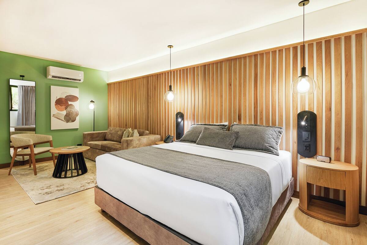Un dormitorio moderno con una cama grande, un panel de madera con listones, una mesita auxiliar redonda y una pequeña mesa redonda.