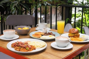 A breakfast table with plates of eggs, bacon, pancakes, and a burger, along with cups of coffee and a glass of orange juice.
