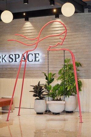 Ein modernes Interieur mit einem Schild, auf dem 'WORK SPACE' steht, Topfpflanzen und einer roten abstrakten Skulptur.