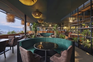 Un espace bar moderne avec des sièges, une vue sur la ville et des plantes d’intérieur.