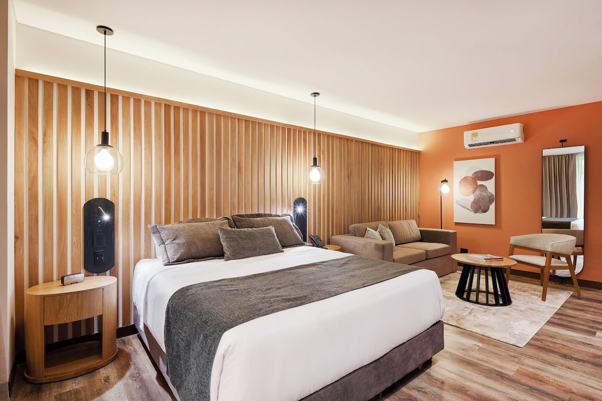 Una habitación de hotel moderna con una cama grande, dos mesitas de noche, un sofá, una pequeña mesa redonda y un aire acondicionado instalado en la pared.