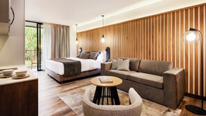 Una habitación de hotel moderna con una cama, un sofá, una pequeña mesa redonda y un escritorio con cuencos.