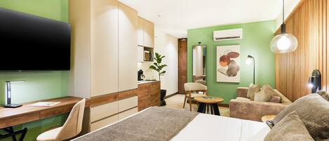 A hotel room with a bed, desk, chair, sofa, and a television.