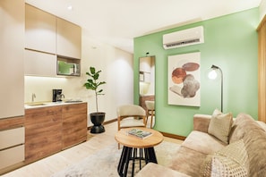 Un salon moderne comprenant un canapé, une table basse, un coin repas agrémenté d’une plante et une cuisine équipée d’un four à micro-ondes.