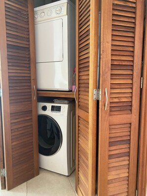 Une buanderie équipée d’un lave-linge et d’un sèche-linge, avec des volets en bois et un sol carrelé.