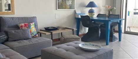 A modern living room with a grey sofa, a blue dining table, and a ceiling fan.