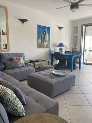 Een moderne woonkamer met een grijze bank, een blauwe eettafel en een plafondventilator.