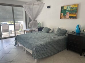 A bedroom with a bed, a nightstand, a bedside table, a wall-mounted artwork, and a sliding glass door leading to an outdoor area. - Simpsonbay Yachtclub apartment with pool (Cole Bay)