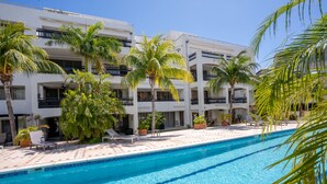 A poolside area with a clear blue pool, palm trees, and a white building with balconies. - Simpsonbay Yachtclub apartment with pool (Cole Bay)