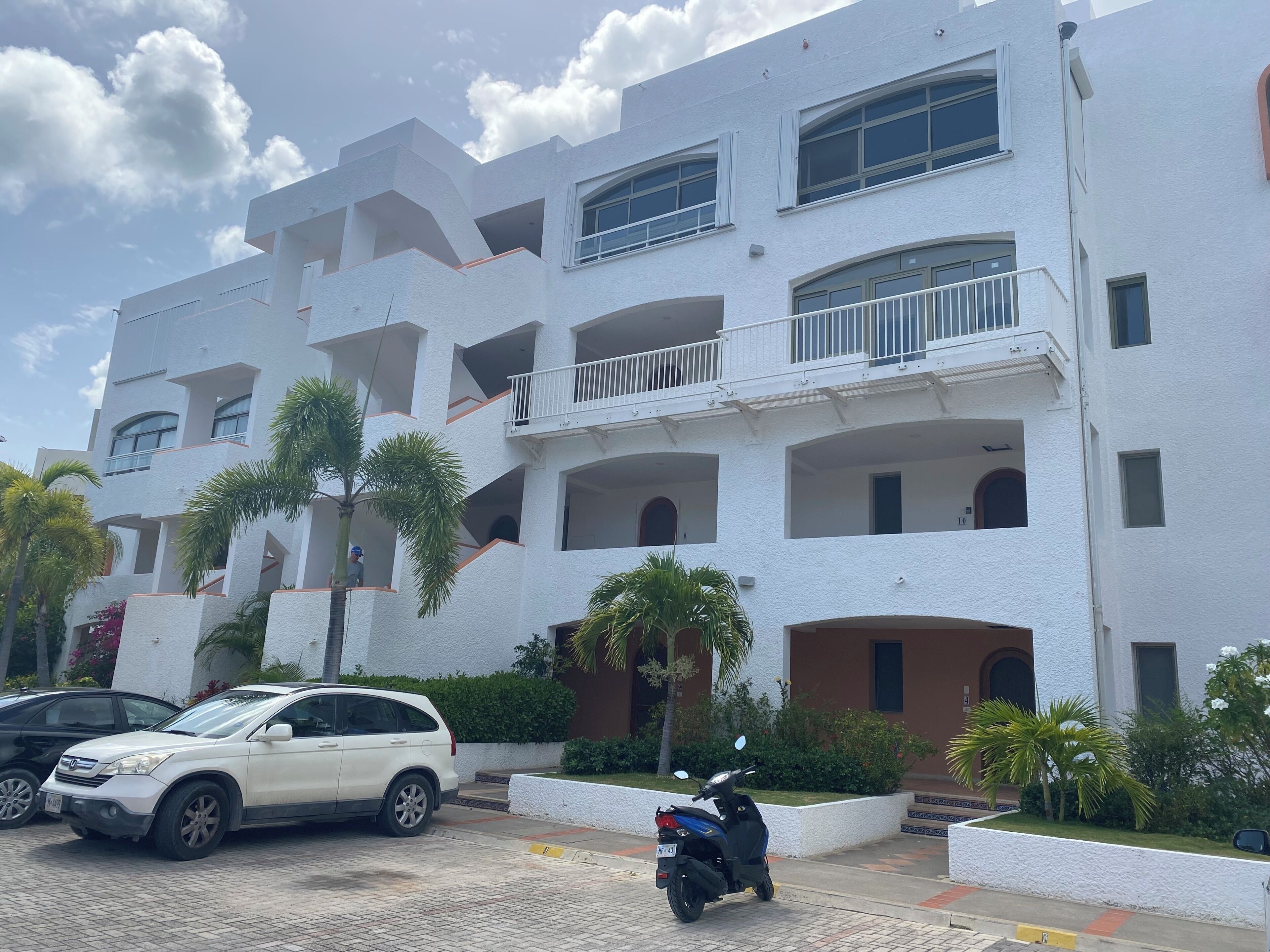 A multi-story building with balconies, a white exterior, and a paved driveway.