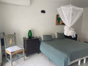 A bedroom with a bed, a nightstand, a chair, a bedside table, a wall-mounted air conditioner, and a painting. - Simpsonbay Yachtclub apartment with pool (Cole Bay)