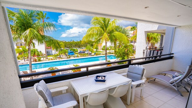 A balcony with a pool view, white furniture, and a small table with a blue tray. - Simpsonbay Yachtclub apartment with pool (Cole Bay)