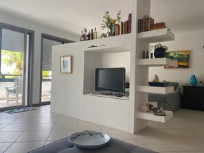 Un salon moderne doté d’un téléviseur à écran plat, d’une bibliothèque et d’un coin repas avec une chaise et une table.
