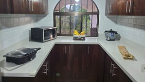 A kitchen with dark wooden cabinets, a white countertop, a microwave, a rice cooker, and a window with a view of trees. - Romantic Rustic Villa in the Mountains 30 Minutes from The  airport . (Barva)