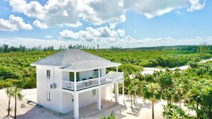 A white two-story house with a balcony, surrounded by palm trees and a beach. - Simple Life Cottage 1 Bedroom Cottage (North Palmetto Point)