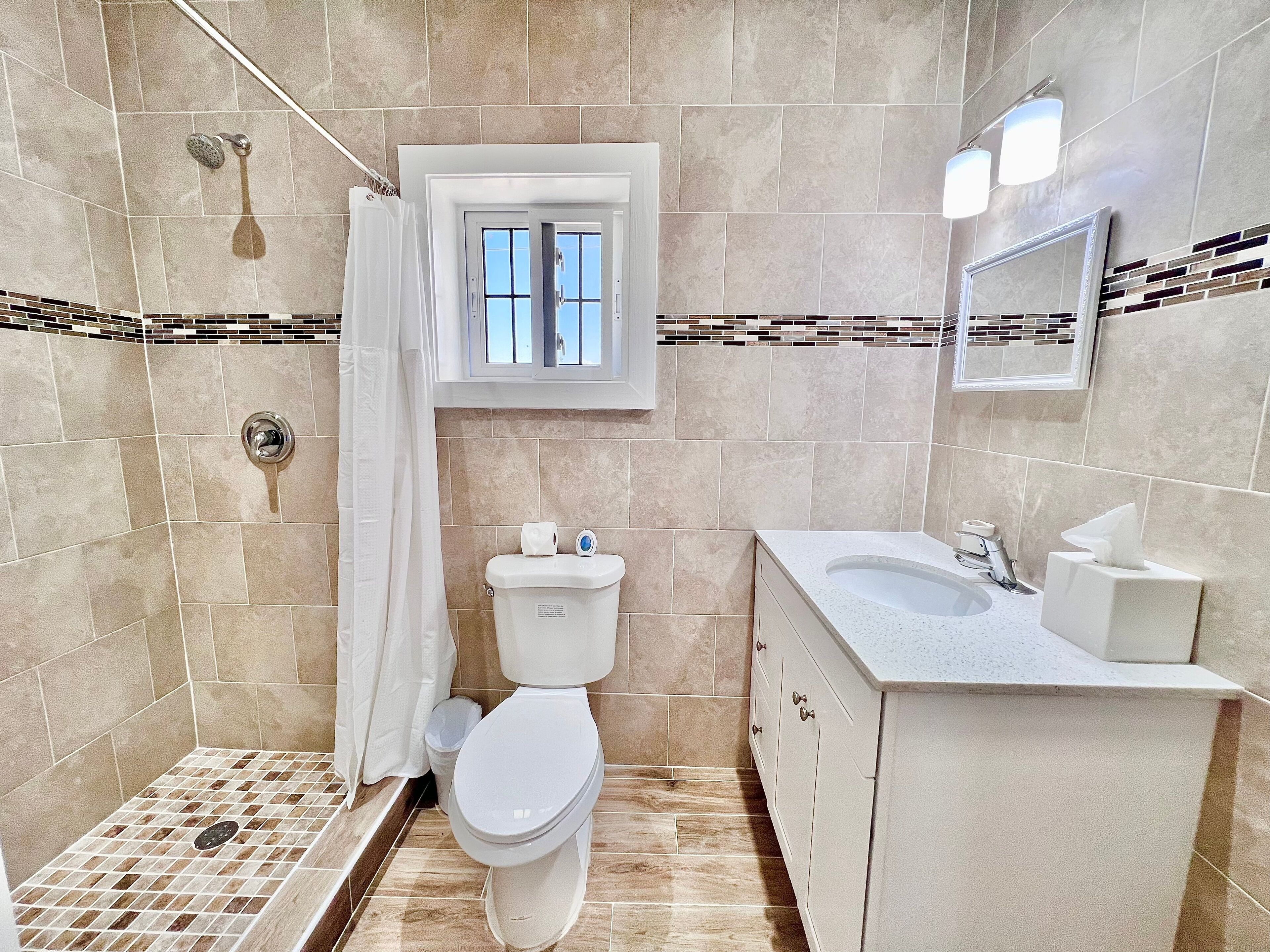 Een badkamer met douche, toilet, wastafel en een raam.