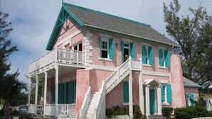 A pink building with white railings and green shutters, featuring a balcony and a staircase leading to the entrance. - Simple Life Cottage 1 Bedroom Cottage (North Palmetto Point)