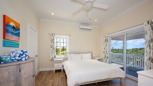 A bedroom with a bed, a nightstand, a dresser, a window with curtains, a ceiling fan, and a view of the outdoors. - Simple Life Cottage 1 Bedroom Cottage (North Palmetto Point)