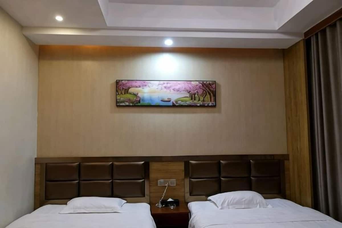 Habitación de hotel con dos camas, cabecero con diseño de panel de madera, un cuadro en la pared y una mesita de noche con lámpara.