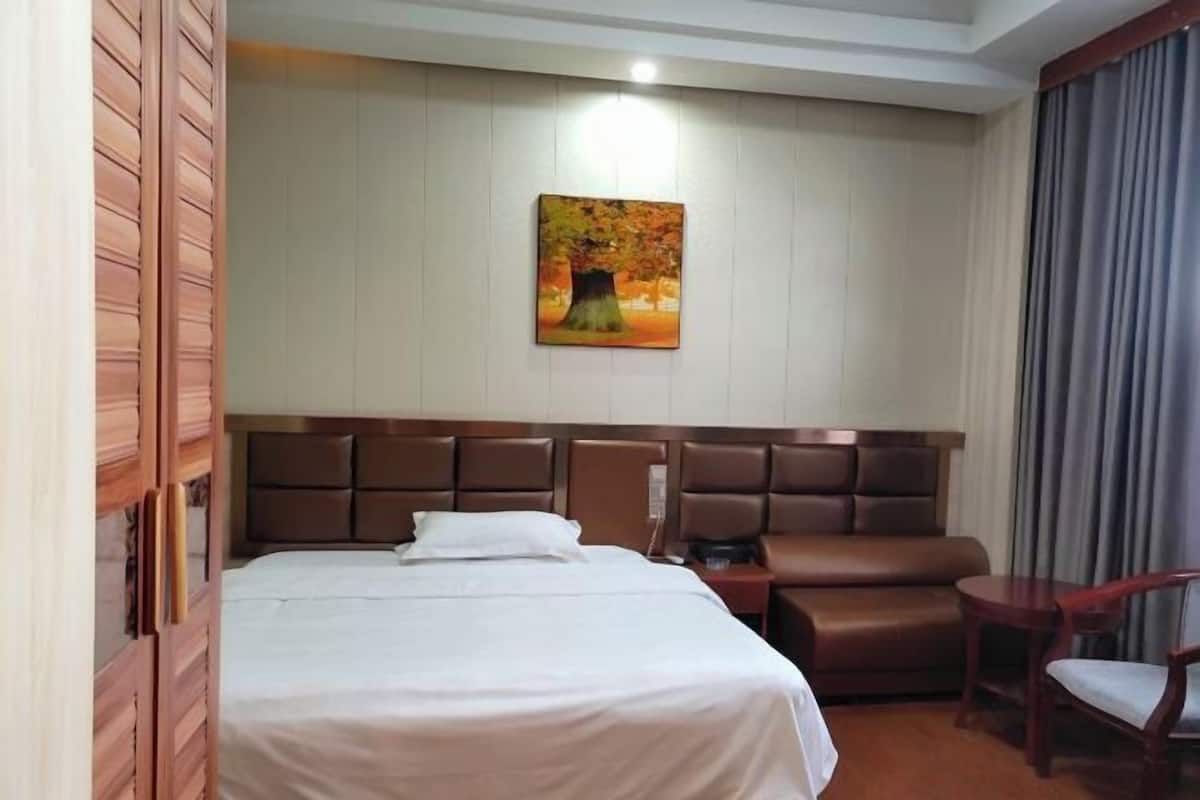 Una habitación de hotel con cama, zona de estar, un cuadro en la pared y ventana con cortinas.
