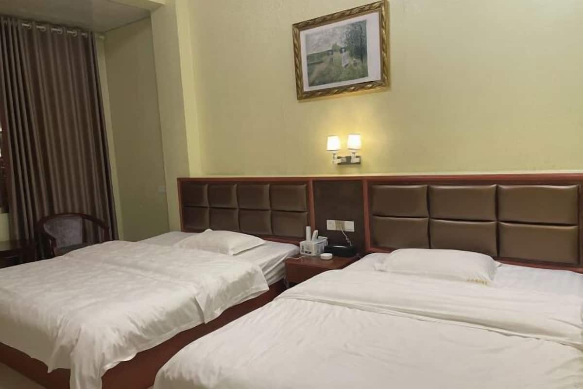Habitación de hotel con dos camas, cabecera con lámpara y un cuadro en la pared.