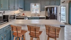 A kitchen with teal cabinets, a stainless steel refrigerator, a central island with bar stools, and a window above the sink. - Gone Fishing on Lake Wateree (Liberty Hill)