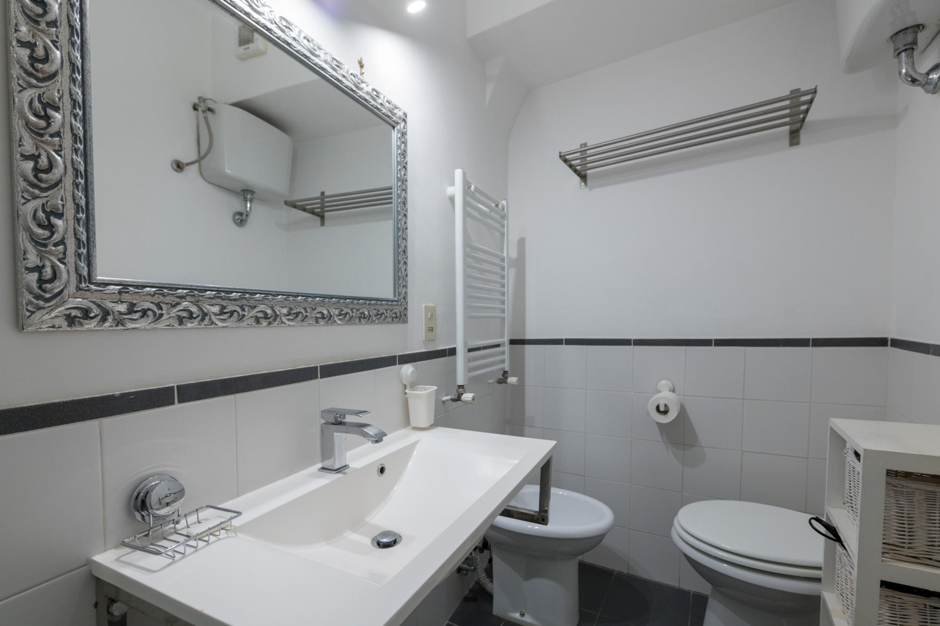 A bathroom with a white sink, a mirror with an ornate frame, a toilet, and a towel rack.
