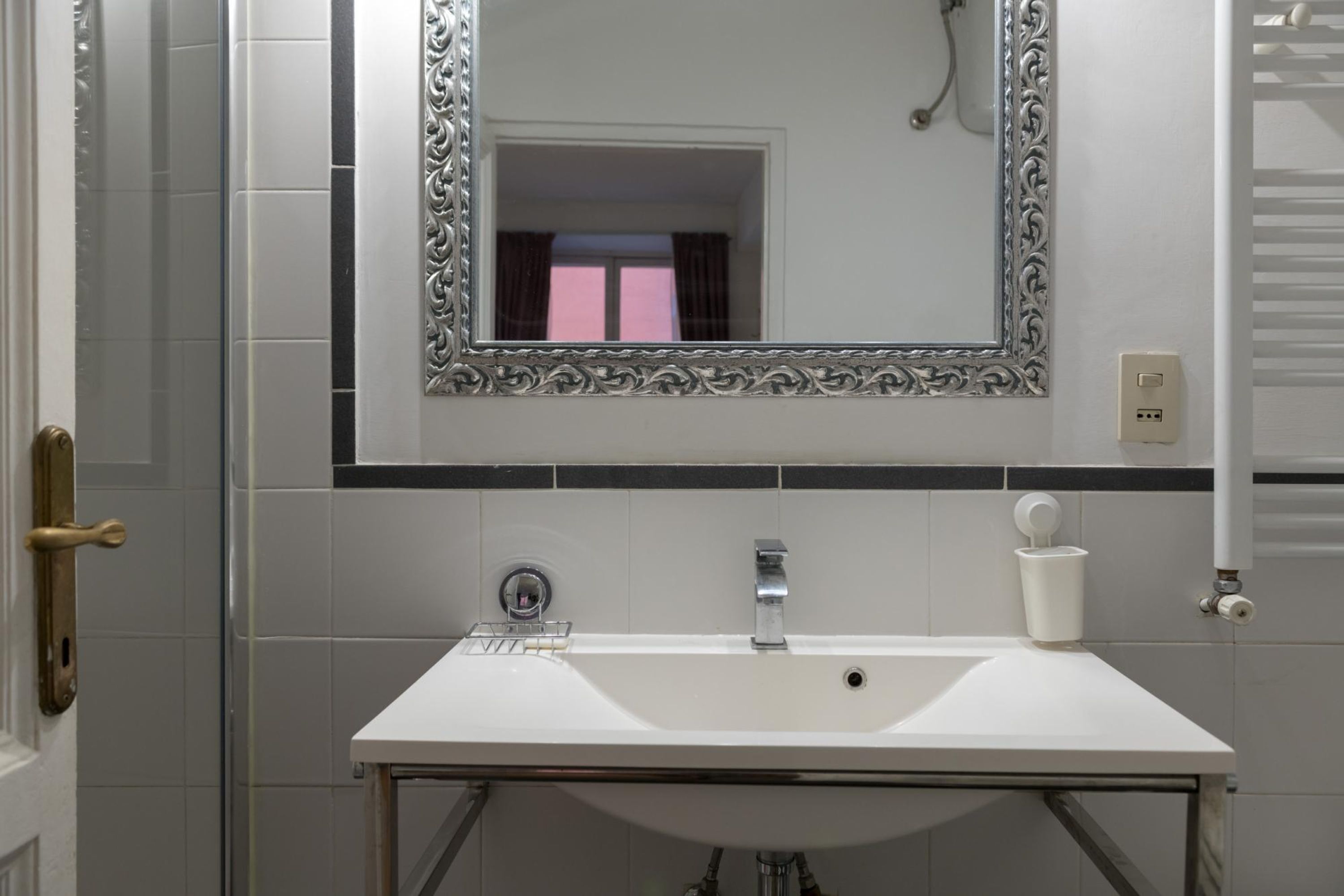 A bathroom with a white sink, a mirror with an ornate frame, and a shower area.