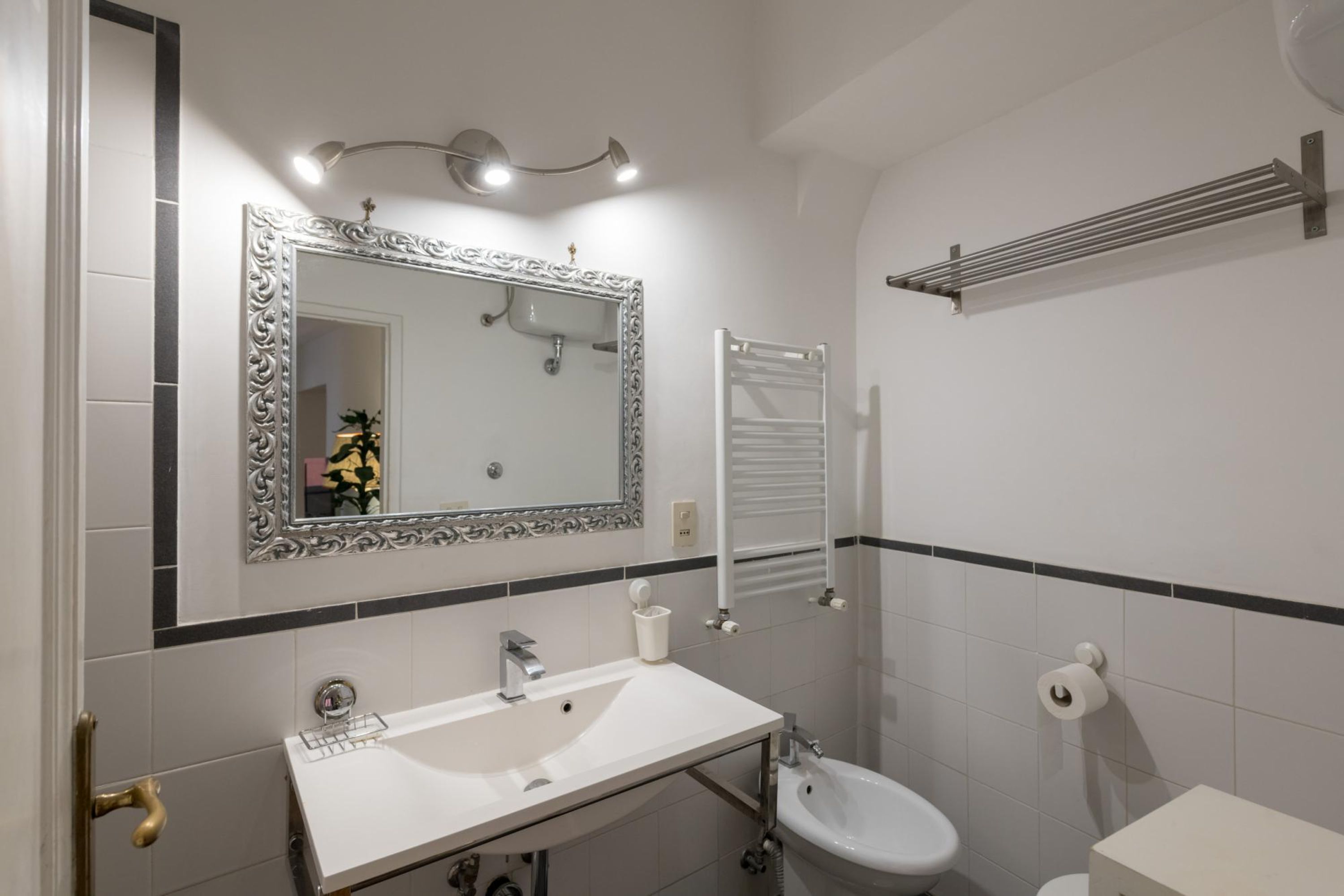 Un baño con lavamanos blanco, un espejo con marco decorativo, toallero y retrete.