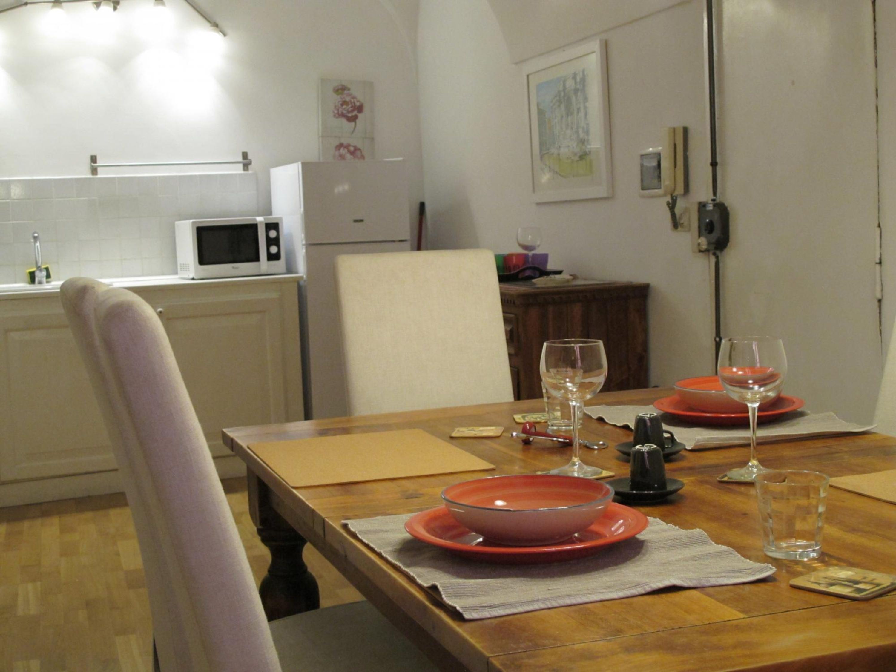 Un coin repas avec une table en bois dressée pour deux personnes, un four à micro-ondes et un réfrigérateur en arrière-plan.