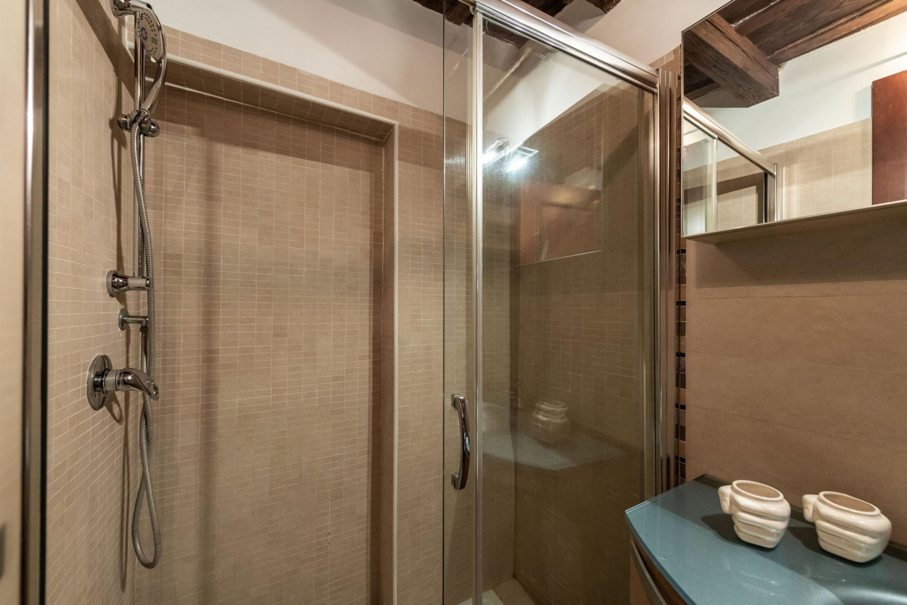 Une douche fermée par des parois en verre, dotée d’un pommeau de douche à main et d’un robinet mural.