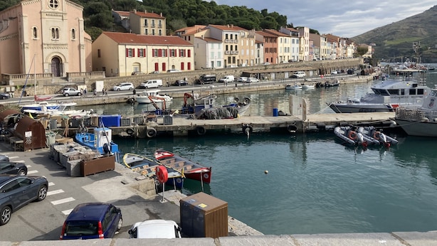 A coastal town with a prominent church, a marina with boats, and a row of colorful buildings along the waterfront.