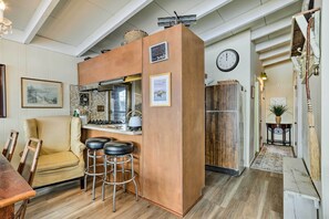 Une cuisine chaleureuse avec un îlot central en bois, des tabourets de bar, un coin repas avec une chaise jaune et une horloge au mur.