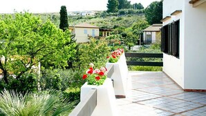 A balcony with a tiled floor, surrounded by greenery and a view of houses in the background. - Villa with swimming pool with spectacular sea views and Mediterranean vegetation (Sicilia)