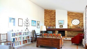 A living room with a fireplace, bookshelves, a sofa, and a red armchair. - Villa with swimming pool with spectacular sea views and Mediterranean vegetation (Sicilia)