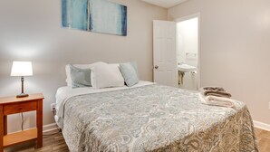 Un dormitorio con cama, mesita de noche, lámpara y un cuadro en la pared.