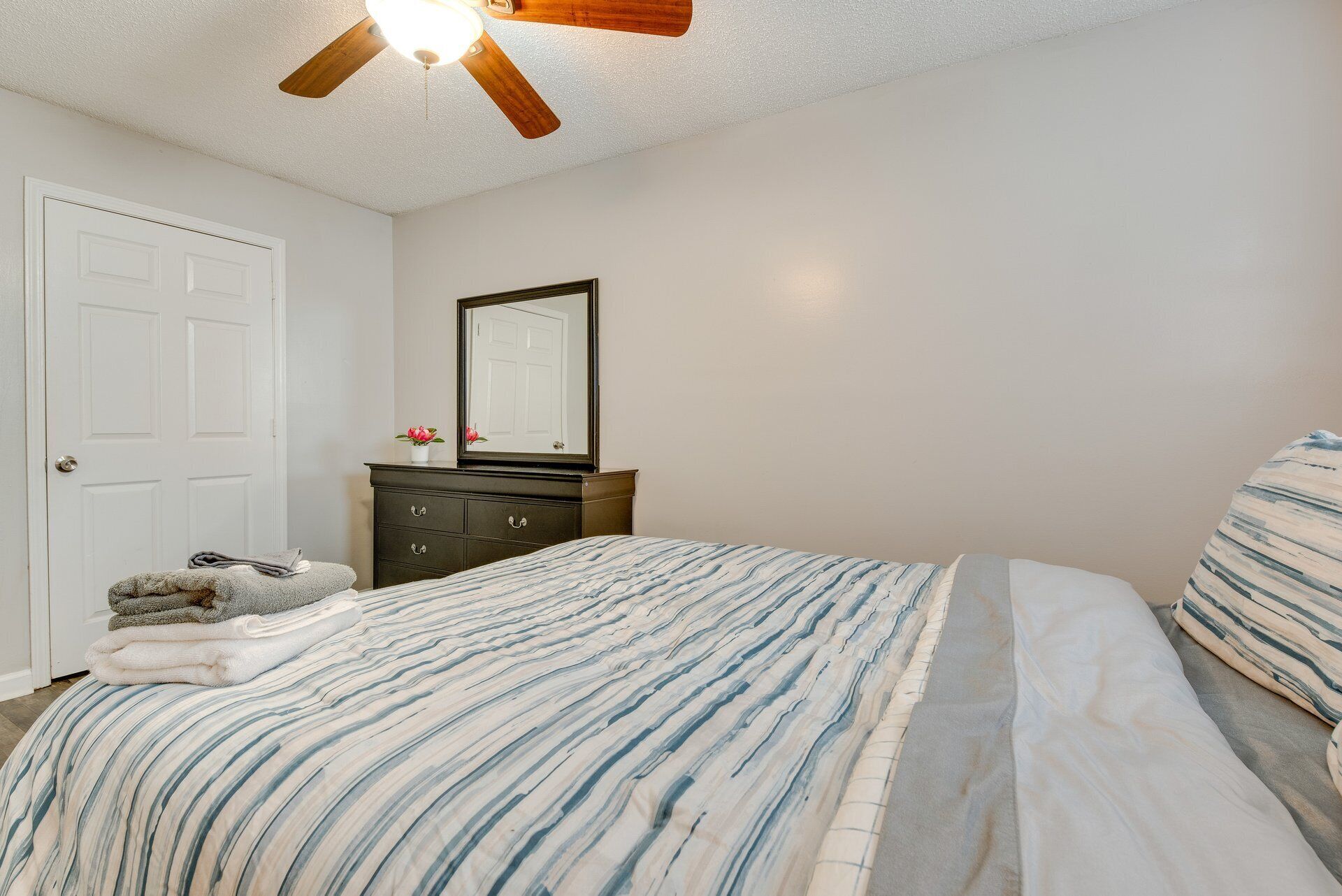 A bedroom with a bed, a dresser, a mirror, and a ceiling fan.