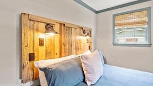 Ein Schlafzimmer mit einem hölzernen Kopfende, zwei Nachttischlampen und einem Fenster mit Jalousien.