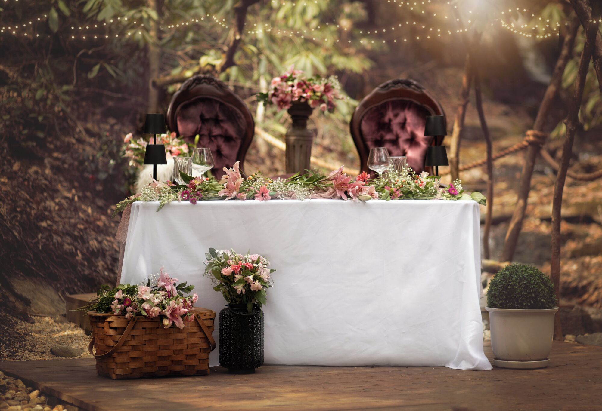 Una mesa cubierta con un mantel blanco, rodeada de sillas y decorada con flores y una pequeña planta en maceta.